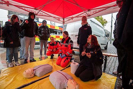 DRK-Mitarbeiterinnen knieen vor Wiederbelebungspuppen und erklären den Umstehenden die Maßnahmen