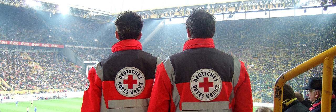 2 Menschen in Einsatzkleidung bei einem Fußballspiel im Stadion.