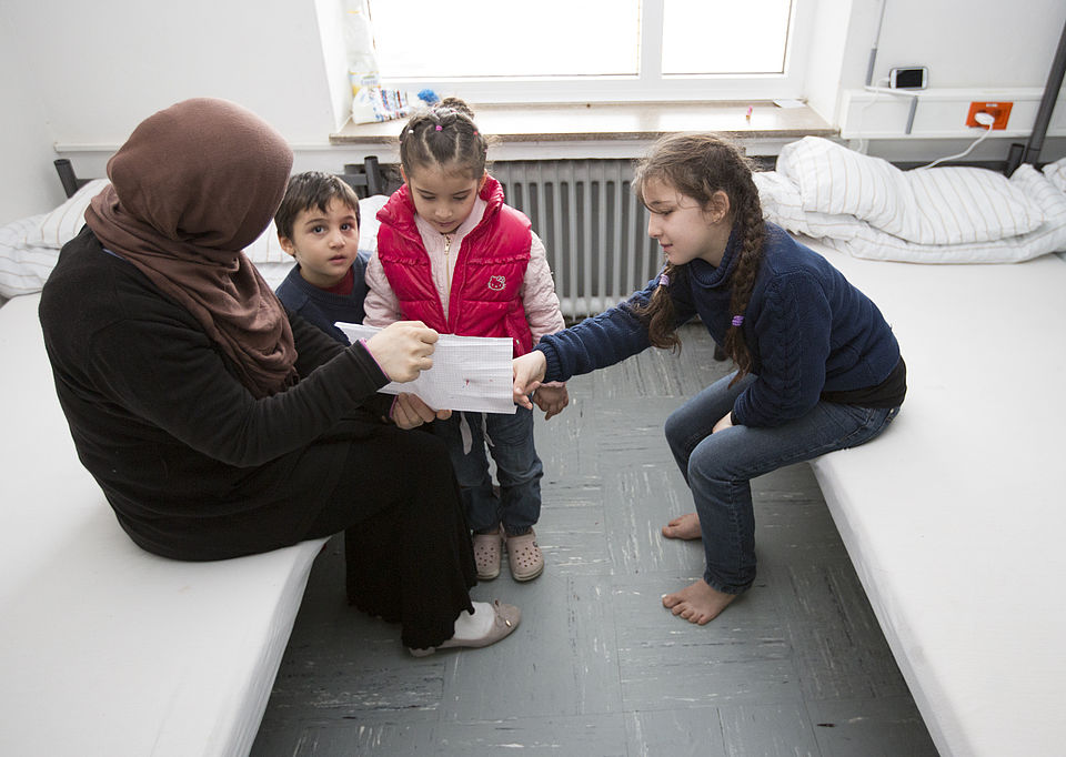 Frau mit Kopftuch sitzt mit drei Kindern auf einem Bett