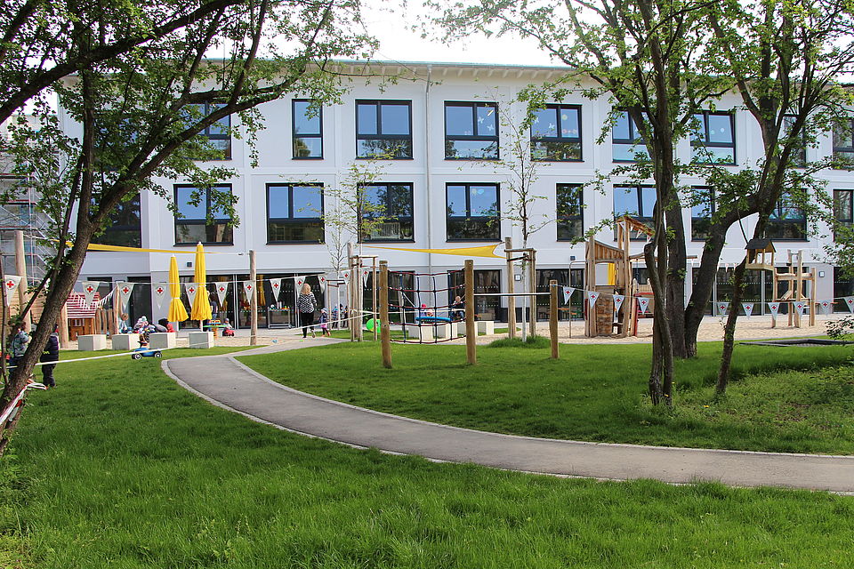 großer Garten mit Spielplatz, im Hintergrund modernes 3-stöckiges Kita-Gebäuse