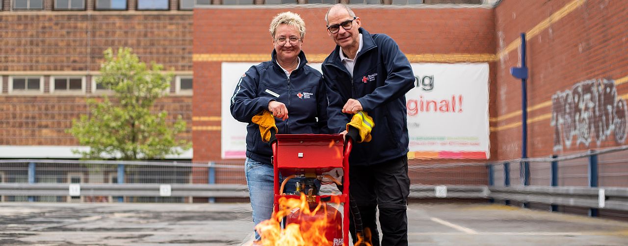 2 Personen stehen hinter einem brennenden Brandschutztrainer-Gerät