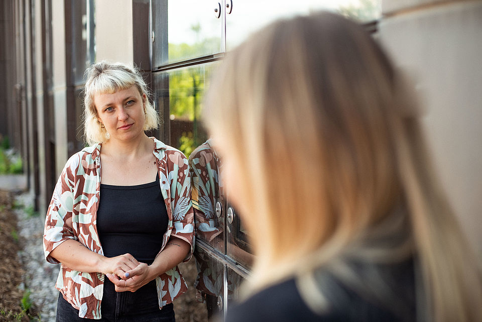 zwei Frauen stehen an eine Hausfassade gelehnt und unterhalten sich